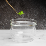Matcha powder being scooped into a glass chawan