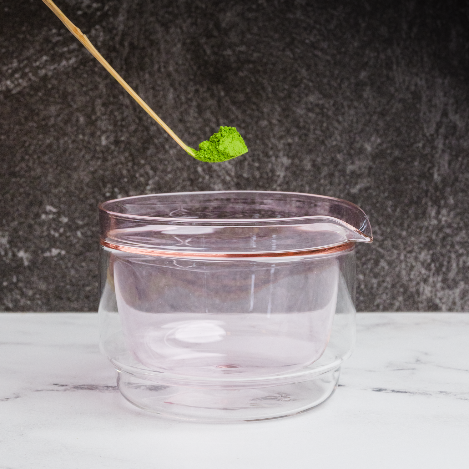 A matcha scoop with matcha powder above a glass container