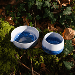 A handmade, ceramic matcha katakuchi chawan bowl and cup with blue interior on a natural background of leaves and moss