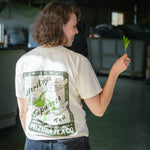 Woman wearing a custom illustrated shirt with Japanese tea design holds a fresh tea leaf from the fields of Japan