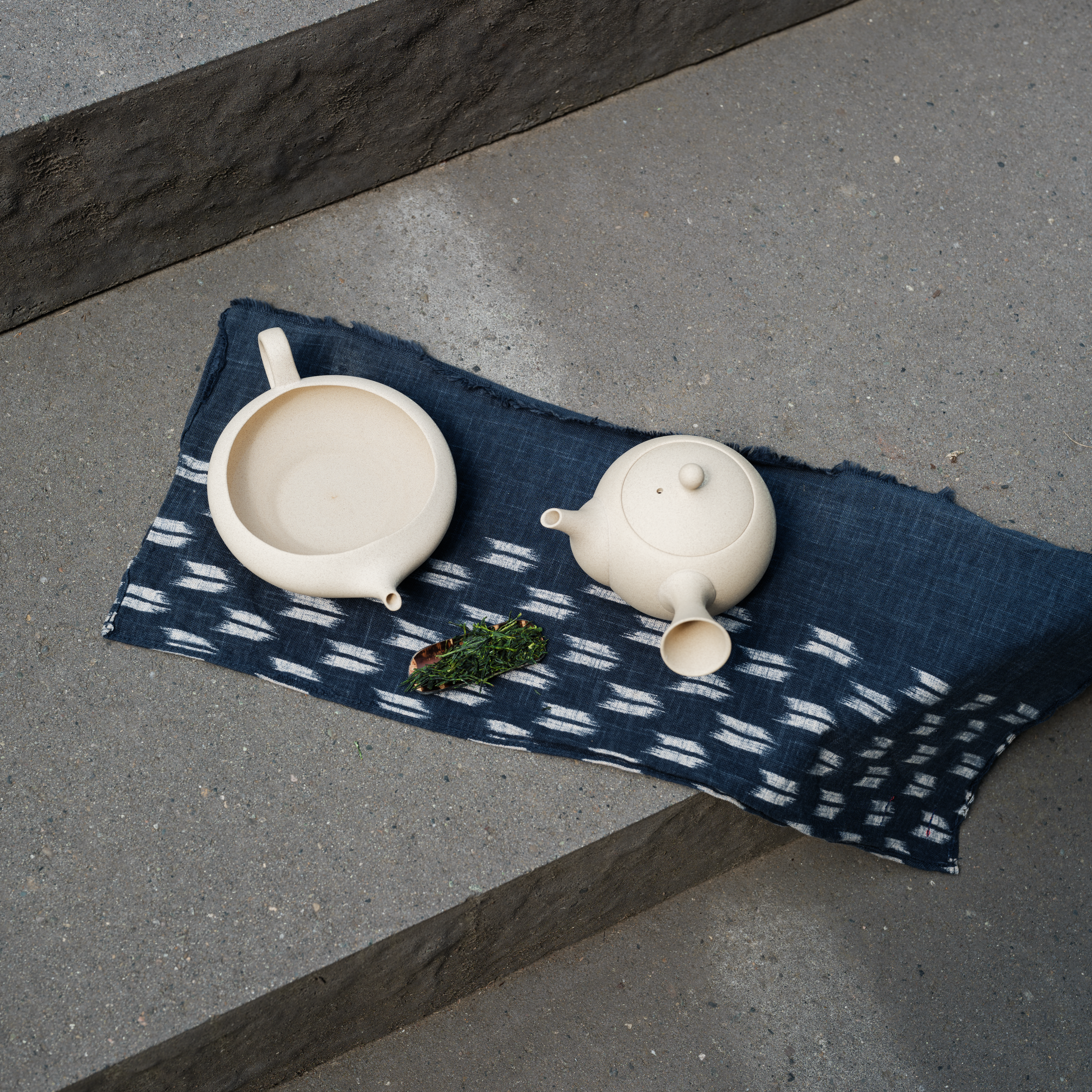 One white ceramic teapot and white ceramic yuzamashi on a blue patterned cloth with a concrete surface.