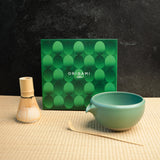 A chasen, chawan, and matcha bowl in front of a green box labeled "Origami Tea"