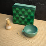 A chasen, chawan, and matcha bowl in front of a green box labeled "Origami Tea"