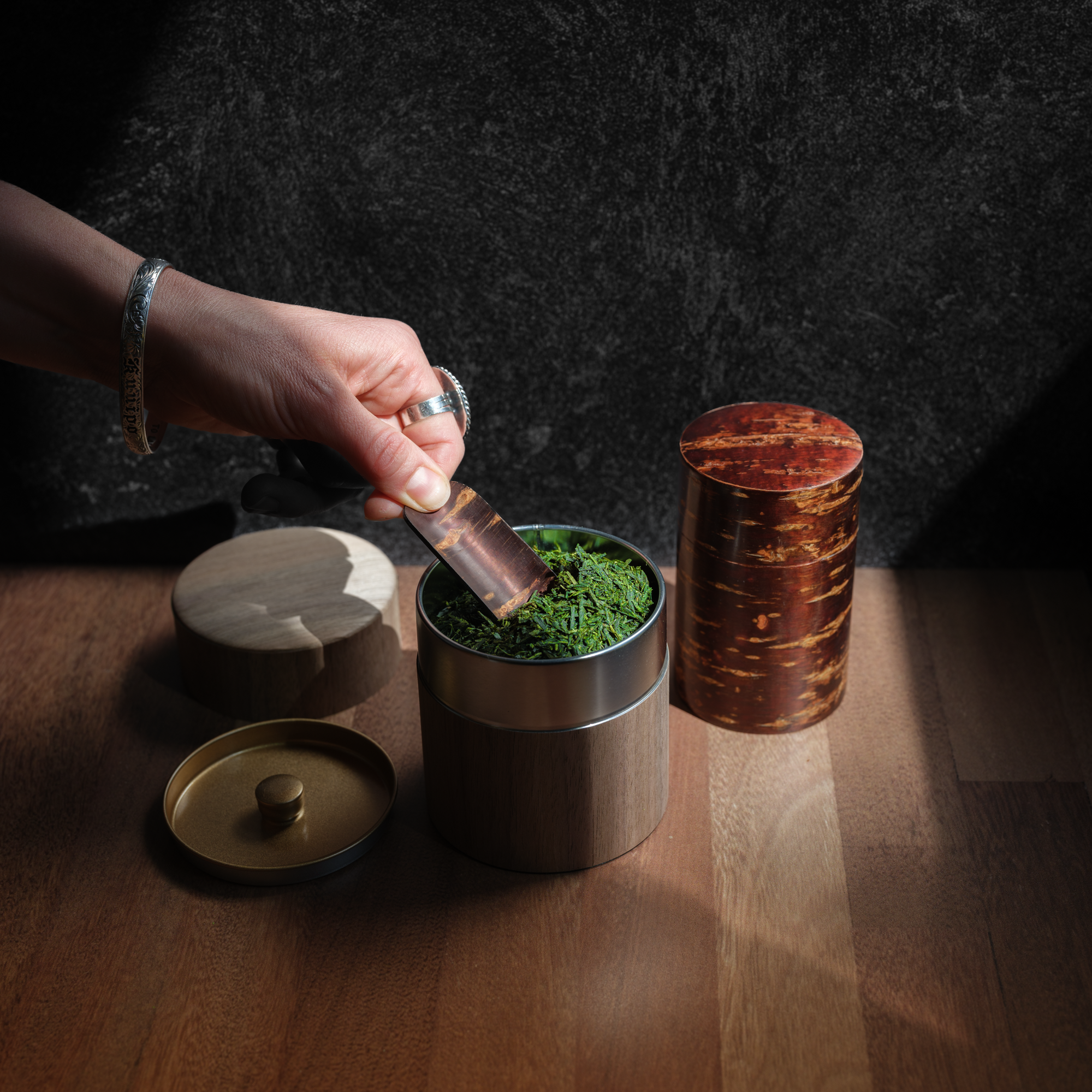 Person uses a cherrywood chasaji tea scoop to lift tea leaves out of the canister.