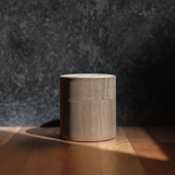 Walnut wooden cylindrical tea canister sits on a wooden surface with a dark textured background.