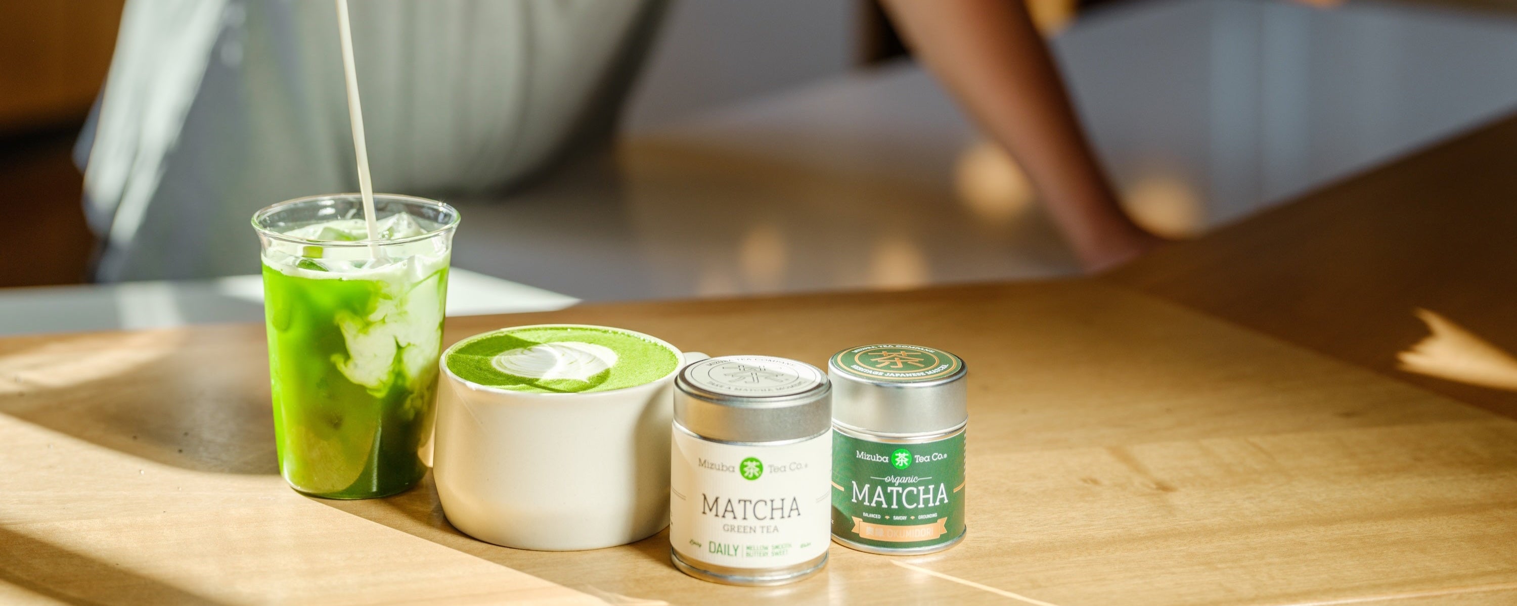 Matcha prepared in glass and tea bowl next to Mizuba Matcha Tins